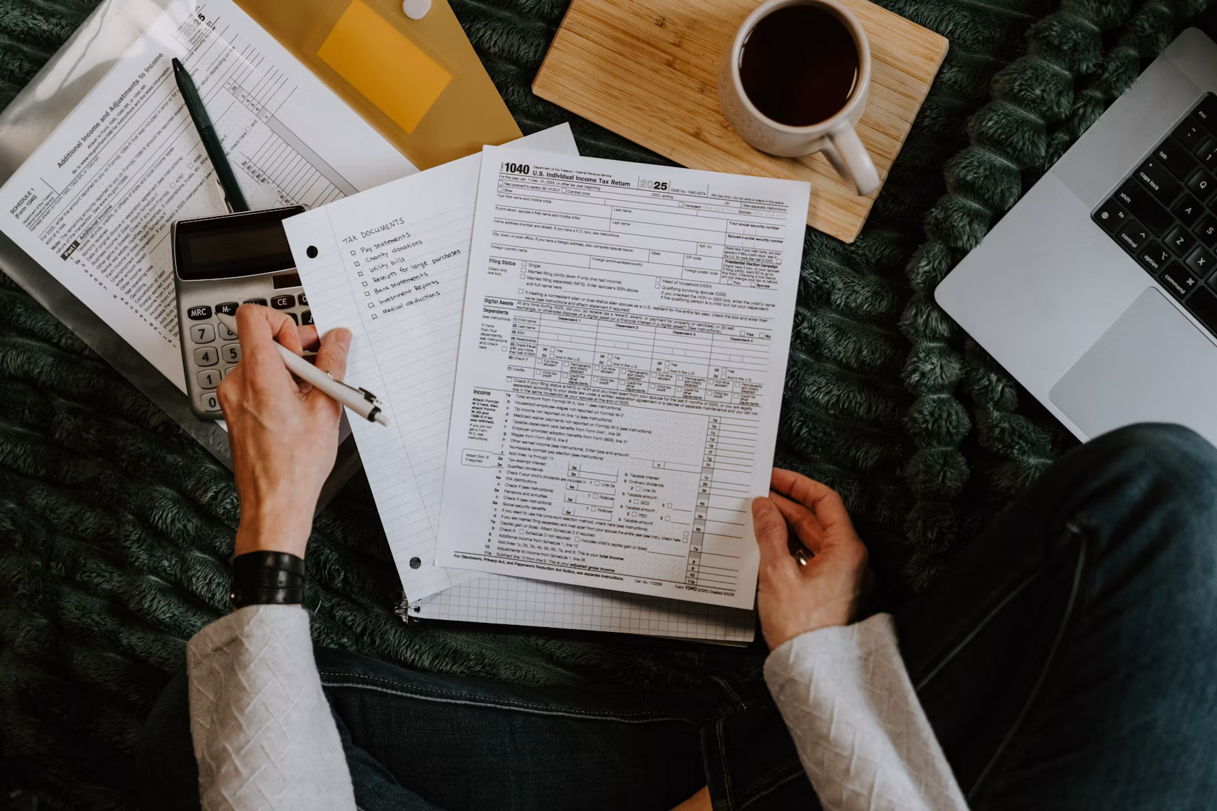 Hands reviewing financial documents beside a calculator and laptop