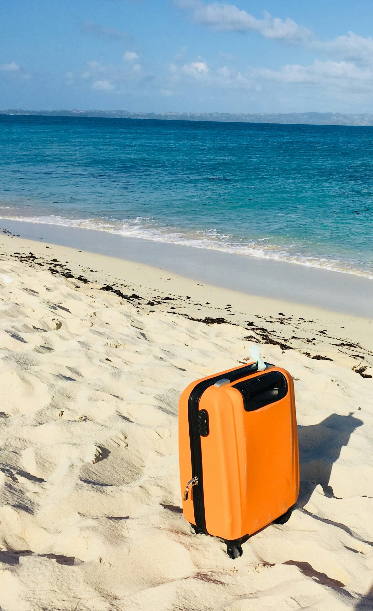 Orange suitcase standing on a sandy beach