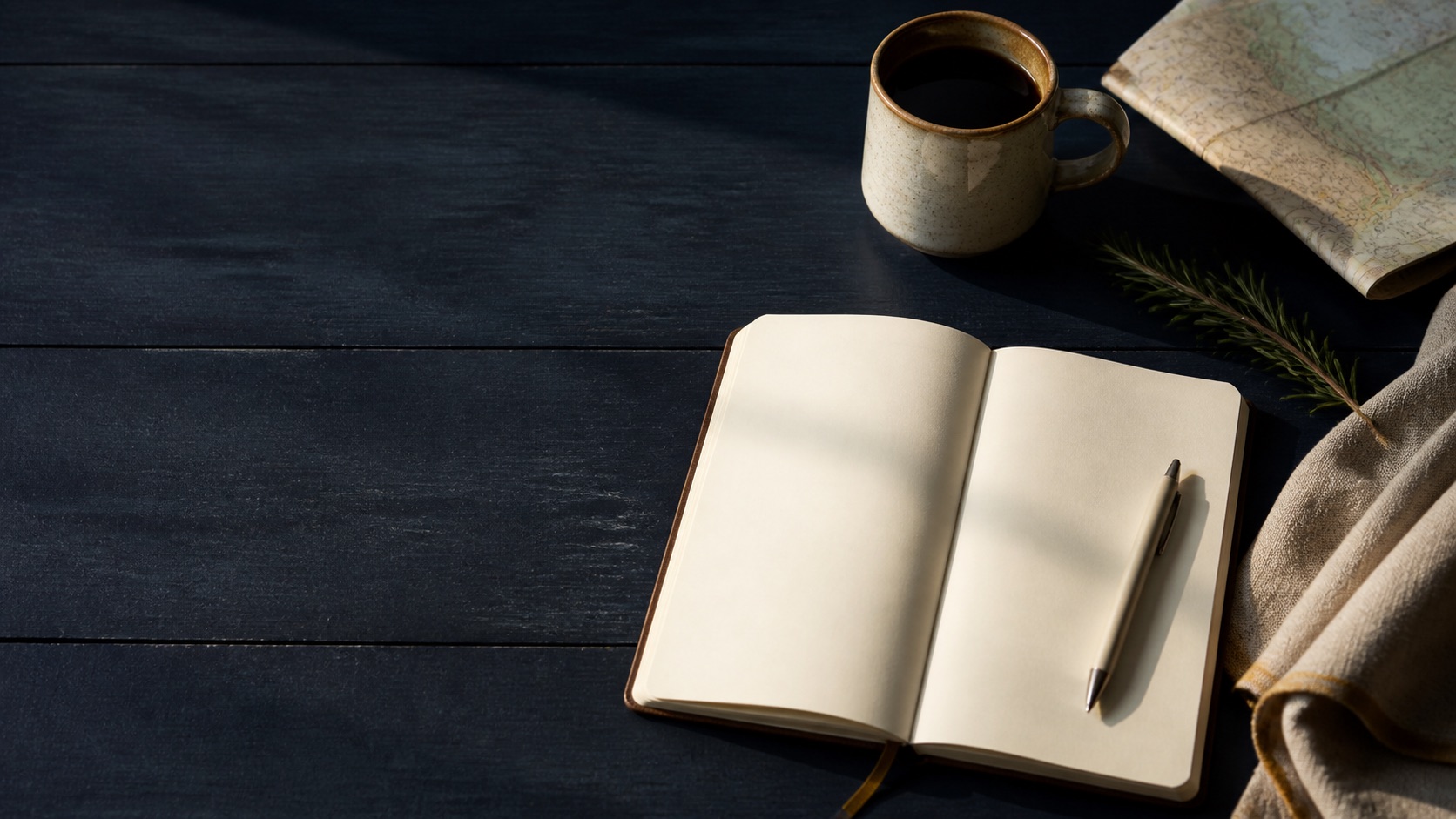 Blank notebook, coffee and folded walking map on a deep navy table