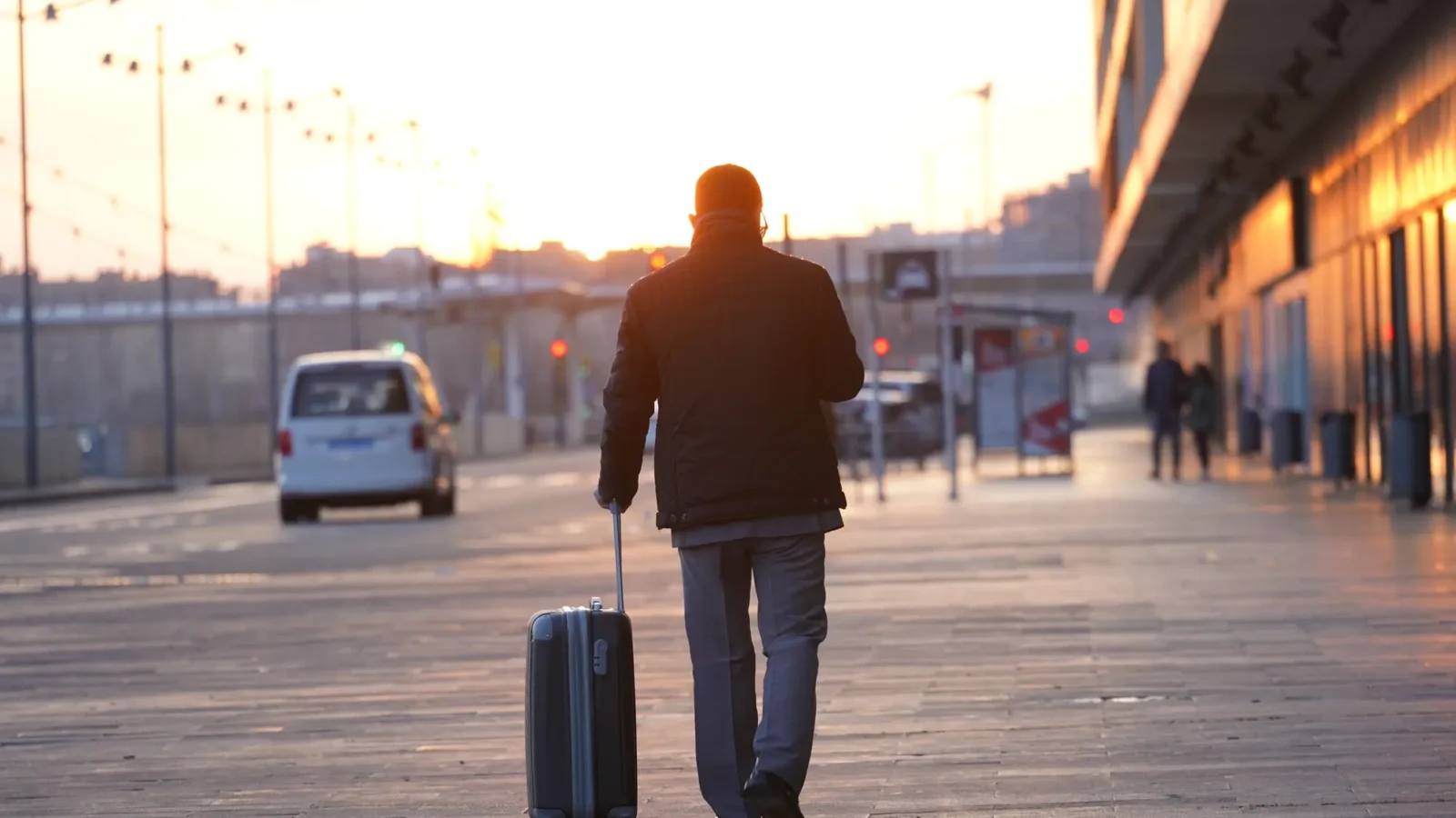 Traveller pulling a wheeled suitcase beside a station at sunset