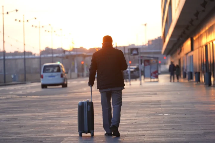 Traveller pulling a wheeled suitcase beside a station at sunset